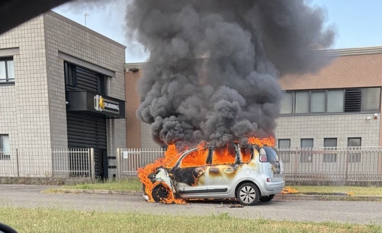 Fiamme avvolgono un’auto, fumo nero nel cielo
